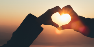 hands making a heart shape in front of a sunset